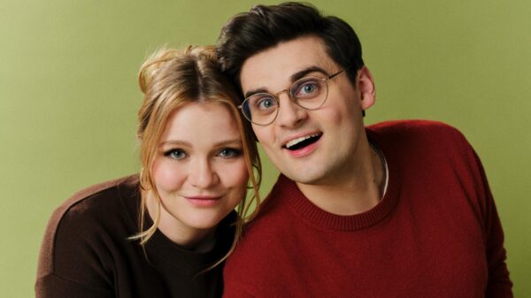 Blonde Frau und Mann mit Brille posieren eng beieinander vor grünem Studiohintergrund.